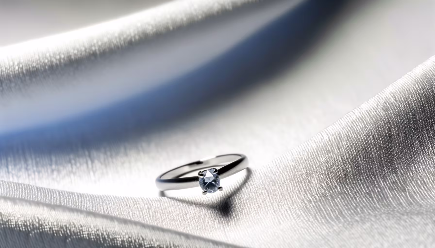 Ein silberner Ring mit einem ovalen, hellblauen Edelstein liegt auf einem glänzenden weißen Stoff.