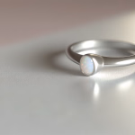 Ein silberner Ring mit einem schillernden Opalstein liegt auf einer hellen Oberfläche.