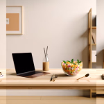 Dieser aufgeräumte und einladende Arbeitsbereich auf einem hellen Holztisch verbindet Produktivität mit gesunder Ernährung und einer beruhigenden Ästhetik. Im Zentrum steht ein geöffneter Laptop, der zum konzentrierten Arbeiten einlädt, begleitet von einer Flasche mit einem cremefarbenen Getränk und stilvollem Besteck. Direkt daneben lockt eine transparente Schale voller farbenfrohem Obstsalat, verziert mit frischer Minze, als nahrhafter Snack. Auf der linken Seite des Tisches sorgt eine kleine, grüne Topfpflanze auf einem Stapel Tellern für einen natürlichen Akzent und frische Luft. Rechts rundet eine Teetasse auf einem Notizbuch die Szenerie ab und suggeriert einen Moment der Ruhe und Reflexion. Der helle, minimalistische Hintergrund mit einem gerahmten Bild und einem Holzregal unterstreicht die ruhige und inspirierende Atmosphäre dieses modernen Raumes, ideal für kreatives Schaffen und Wohlbefinden. **Alternativtext:** Ein heller Holztisch mit einem Laptop, einer Schale Obstsalat, einer Pflanze und einer Teetasse, in einem modernen Raum mit minimalistischer Einrichtung.