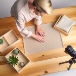 Eine Frau richtet Deko-Elemente wie Stoffe und Sukkulenten auf einem Holztisch ein, während eine Kamera auf einem Stativ die Szene filmt.