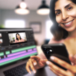 Eine lächelnde Frau hält ein Smartphone, während ein Laptop vor ihr ein Videobearbeitungsprogramm mit Clips einer Frau anzeigt.