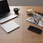 Ein Holztisch mit einem Laptop, einem Notizbuch, zwei Tassen Kaffee, einem Magazin und einem Smartphone.