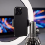 Mobile Videoaufnahme-Einrichtung mit einem Smartphone auf Stativ und Ringlicht, vor unscharfen Bildschirmen.