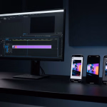 Arbeitsplatz für Videobearbeitung mit einem Monitor, der eine Schnittsoftware anzeigt, und drei Smartphones, die dasselbe bunte Video wiedergeben.