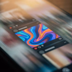 Nahaufnahme eines Smartphones, das einen Social-Media-Feed anzeigt, mit einem prominenten Beitrag eines farbenfrohen, abstrakten Bildes aus fließenden blauen, orangefarbenen und violetten Tönen.