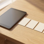 **Vorgeschlagener Text:** In einer zunehmend digitalen Welt finden wir oft Inspiration und Effizienz in der Kombination von Technologie und traditionellen Methoden. Dieses Bild fängt genau diese Synergie ein: ein modernes Tablet neben einer Reihe von leeren Karten, die bereit für Ideen, Notizen oder Designkonzepte sind. Es erinnert uns daran, dass die besten Lösungen oft entstehen, wenn wir das Beste aus beiden Welten nutzen – die unendlichen Möglichkeiten der digitalen Welt und die greifbare Klarheit physischer Hilfsmittel. Ob für Projektplanung, kreatives Brainstorming oder die Gestaltung von Moodboards, die Vereinigung von digitaler Präzision und analoger Flexibilität kann Ihren Arbeitsablauf revolutionieren. **Alternativtext:** Ein Tablet mit dunklem Bildschirm und vier leere weiße Karten liegen auf einem hellen Holztisch, der teilweise von Sonnenlicht beleuchtet wird.