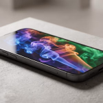 Ein modernes Smartphone liegt auf einer hellgrauen Oberfläche und zeigt auf seinem Bildschirm ein lebhaftes, abstraktes Rauchbild in Blau-, Lila-, Orange- und Grüntönen.