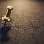 Eine goldene Reißzwecke steckt in einer dunklen, filzartigen Oberfläche, um einen wichtigen Punkt oder eine Idee zu markieren.