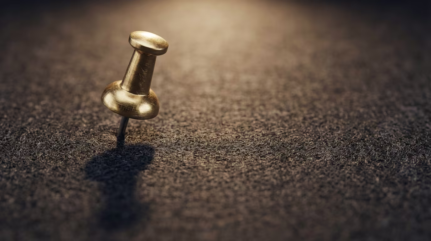 Eine goldene Reißzwecke steckt in einer dunklen, filzartigen Oberfläche, um einen wichtigen Punkt oder eine Idee zu markieren.