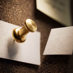 Ein goldener Reißzwecke befestigt ein zerissenes, beiges Blatt Papier an einer Korkwand, mit einem zweiten Stück des Papiers daneben."