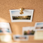 Korktafel mit mehreren Fotos und Notizen, im Vordergrund scharf fokussiert ein Foto einer Landschaft bei Sonnenuntergang.
